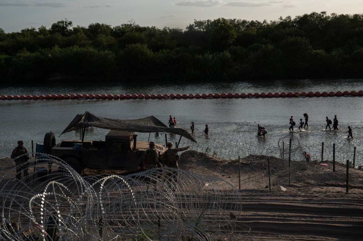 Migrants walk along the Rio Grande past recently installed buoys in Eagle Pass, Texas on July 29, 2023.