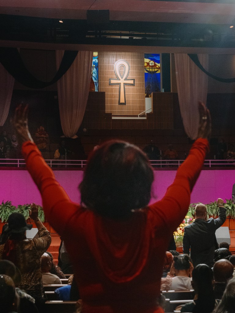 A churchgoer rises and lifts her hands at the end of a sermon.