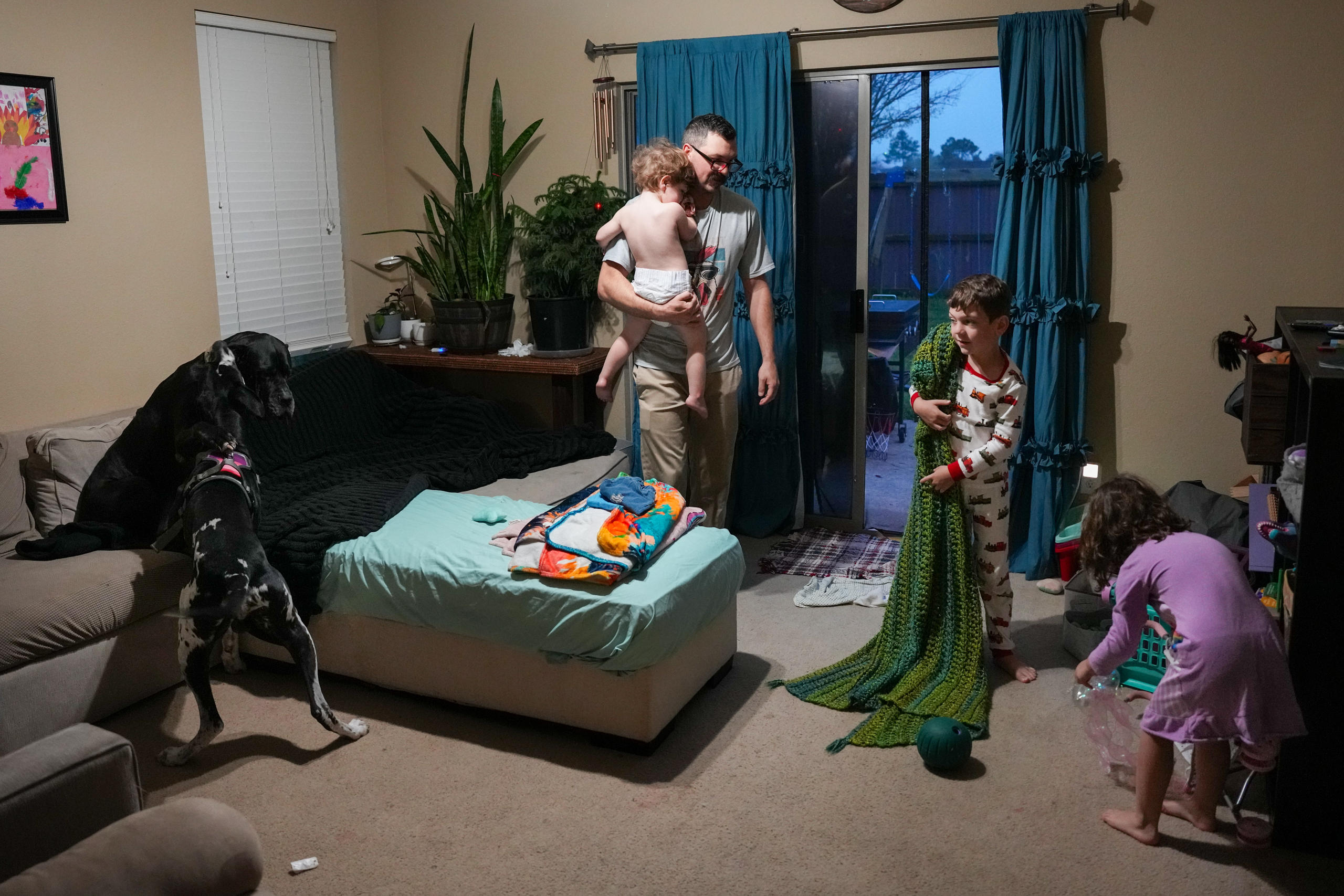 Tony Herzog, center, holds his daughter Olive, 2, as he helps his son Henry, 7, second from right, and daughter Scarlett, 5, at right, start their day on Monday, March 9, 2026, at their home in Manvel.