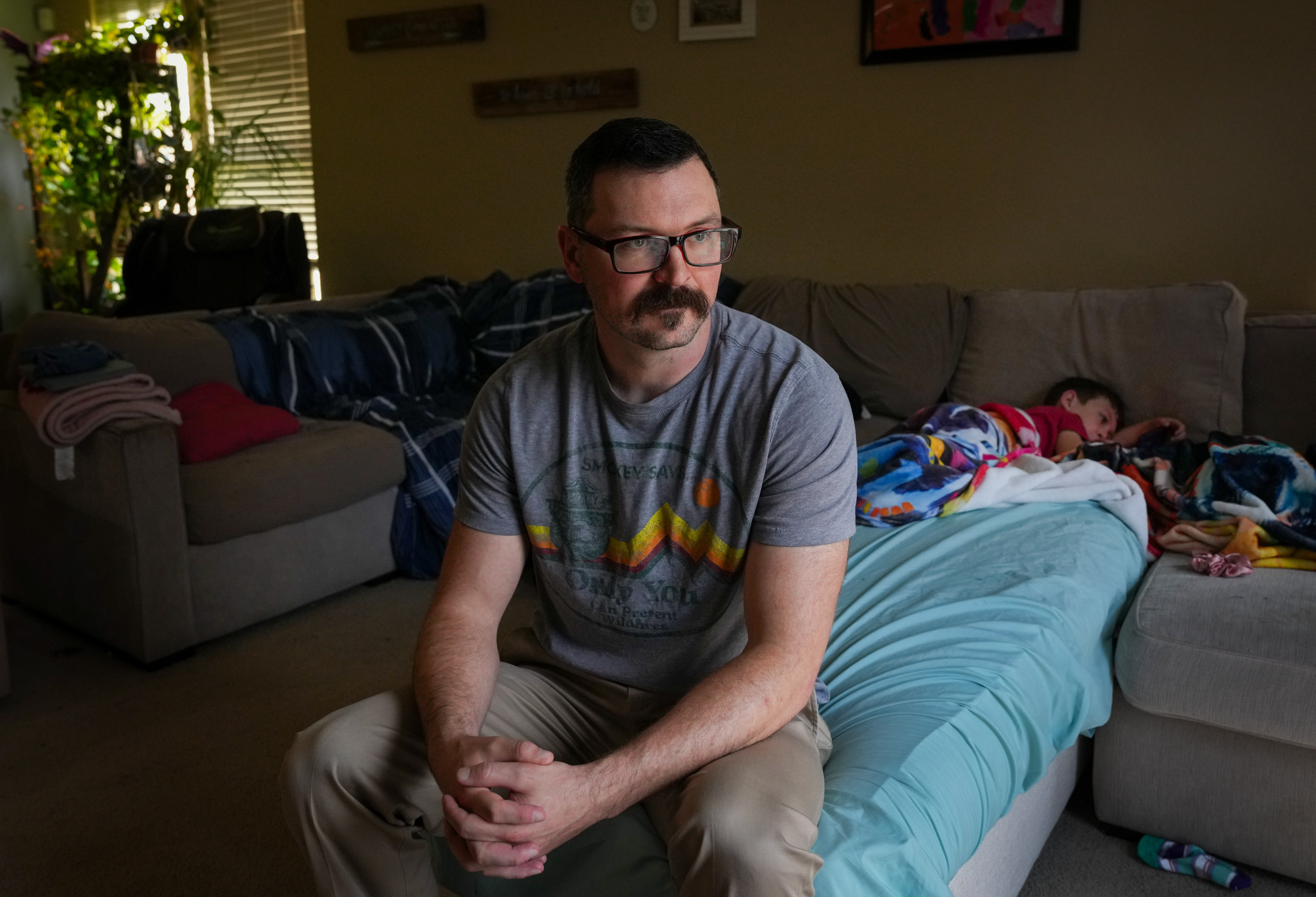 Anthony Herzog poses for a portrait as his son Henry, 7, watches videos on Monday, March 9, 2026, at their home in Manvel.